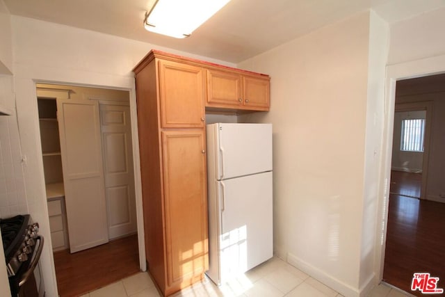 kitchen featuring light brown cabinets, white refrigerator, light wood-type flooring, and gas stove