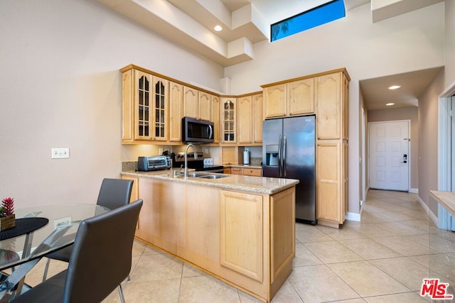 kitchen with light stone counters, light brown cabinets, stainless steel appliances, a high ceiling, and light tile patterned floors