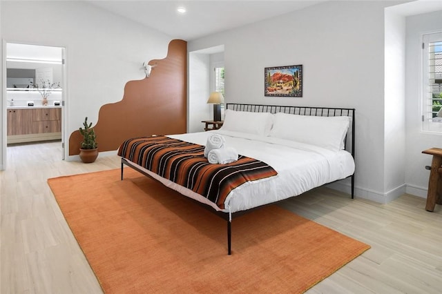 bedroom featuring connected bathroom and light hardwood / wood-style floors