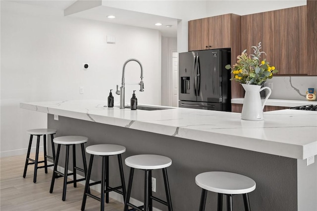 kitchen featuring a breakfast bar, stainless steel fridge with ice dispenser, light hardwood / wood-style floors, and sink