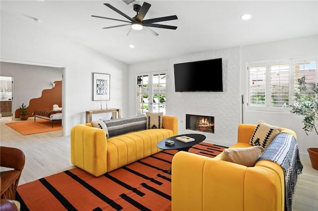 living room featuring a large fireplace, ceiling fan, light hardwood / wood-style flooring, and lofted ceiling