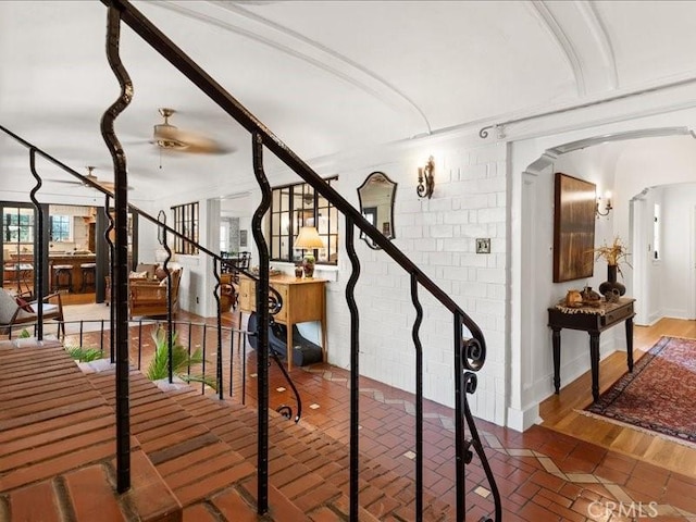 stairway featuring ceiling fan and brick wall