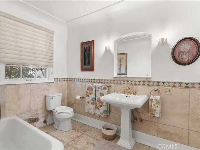 bathroom with a tub to relax in, tile walls, tile patterned floors, and toilet