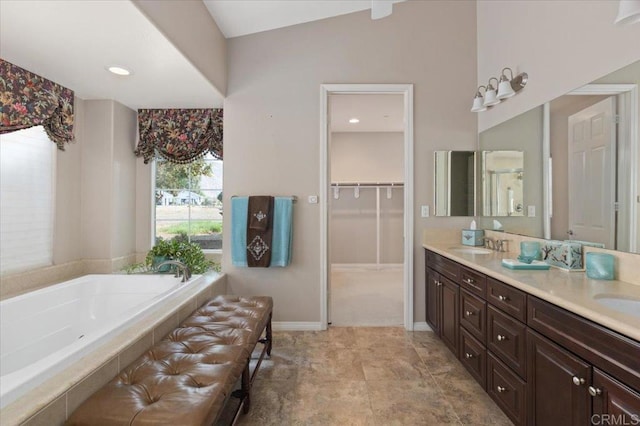 bathroom featuring vanity, a relaxing tiled tub, and vaulted ceiling