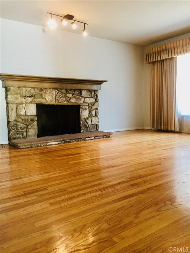 unfurnished living room with a fireplace, rail lighting, and light wood-type flooring