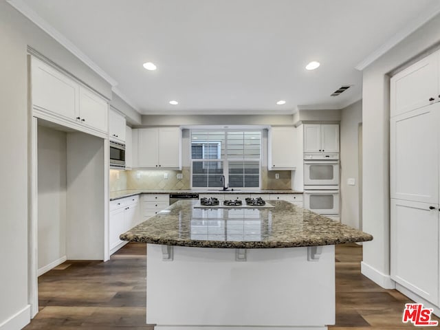 kitchen with double oven, white cabinetry, stainless steel microwave, and a kitchen island