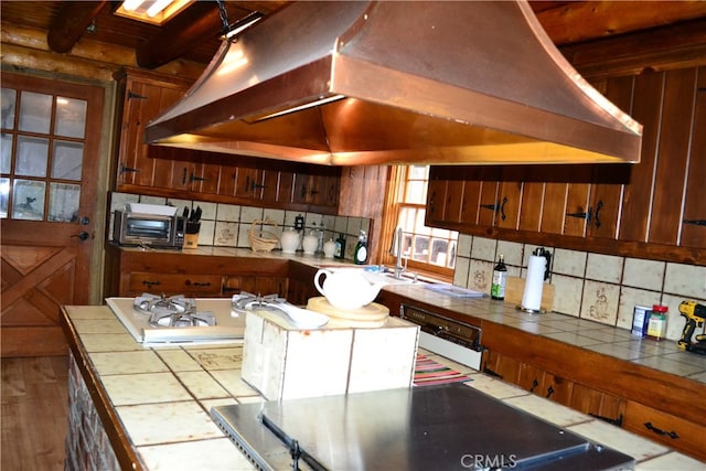 kitchen with custom range hood, backsplash, light wood-type flooring, and tile counters