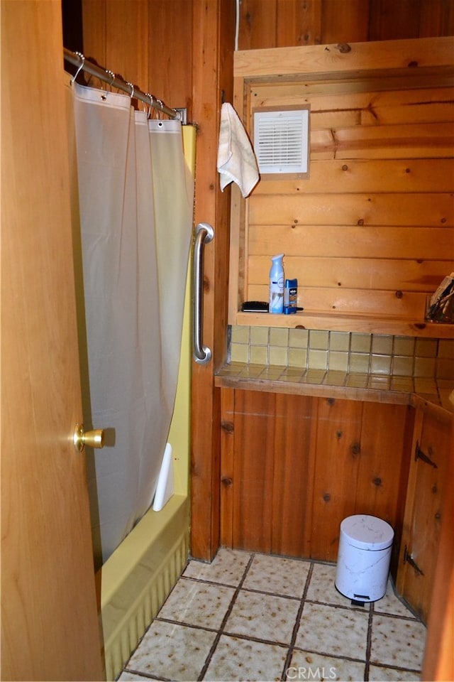 bathroom featuring wooden walls, tile patterned floors, and shower / bath combo