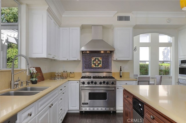 kitchen with stainless steel appliances, white cabinetry, sink, and wall chimney range hood