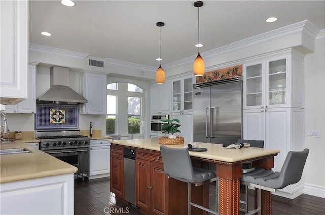 kitchen featuring hanging light fixtures, high end appliances, wall chimney range hood, and white cabinets