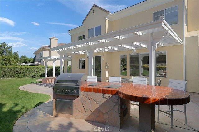 back of property featuring a pergola, a patio area, a lawn, and an outdoor kitchen