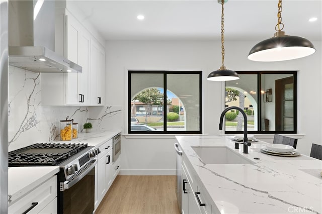 kitchen with appliances with stainless steel finishes, sink, wall chimney range hood, and white cabinetry