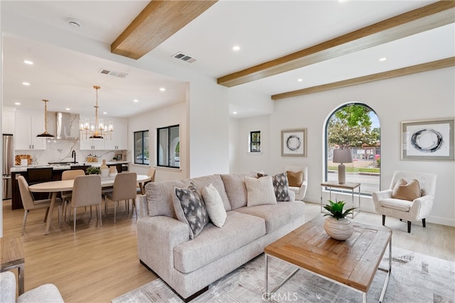 living room with beamed ceiling, an inviting chandelier, and light wood-type flooring