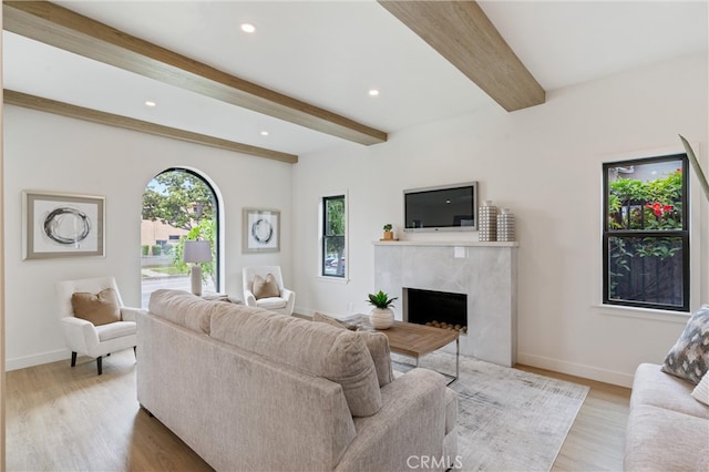 living room featuring a high end fireplace, beamed ceiling, and light hardwood / wood-style flooring