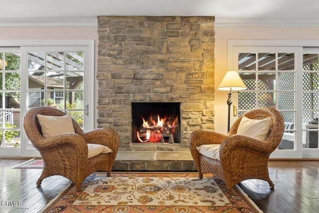 living area featuring hardwood / wood-style floors, ornamental molding, and a stone fireplace