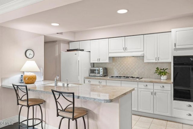 kitchen with white refrigerator, white cabinets, light stone counters, a kitchen breakfast bar, and stainless steel gas stovetop