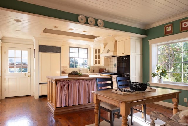 kitchen with backsplash, premium range hood, dark wood-type flooring, crown molding, and paneled refrigerator