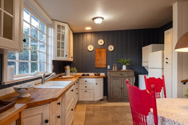 kitchen with wood walls, wooden counters, white refrigerator, sink, and white cabinetry