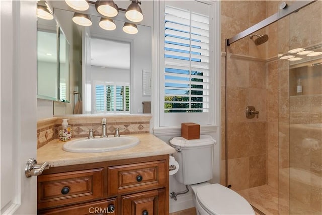 bathroom with vanity, toilet, a shower with door, and decorative backsplash