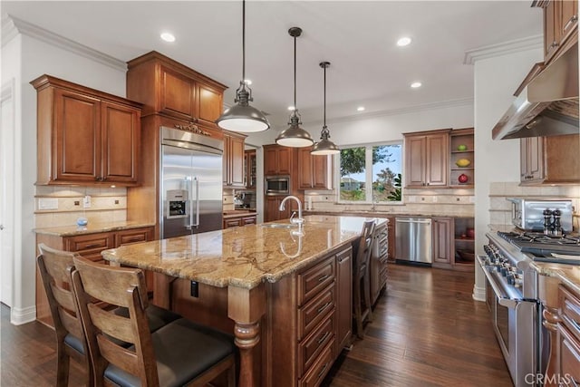 kitchen with a breakfast bar area, decorative backsplash, decorative light fixtures, a kitchen island with sink, and built in appliances