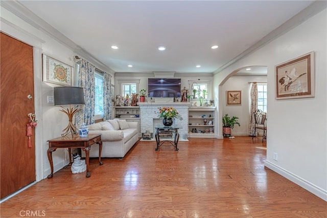 living room with a brick fireplace, light wood-type flooring, crown molding, and a healthy amount of sunlight