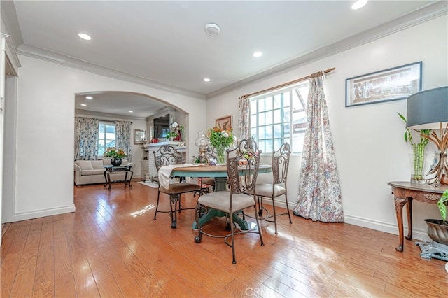 dining space with a stone fireplace, light hardwood / wood-style flooring, and ornamental molding