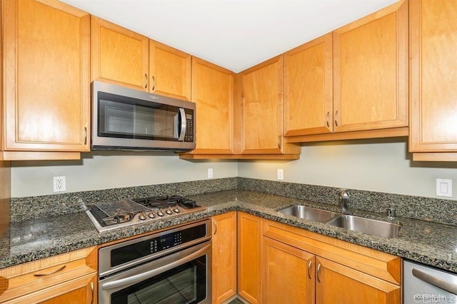 kitchen with appliances with stainless steel finishes, sink, and dark stone counters