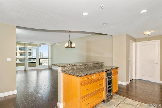 kitchen with wine cooler, light hardwood / wood-style floors, hanging light fixtures, and dark stone countertops