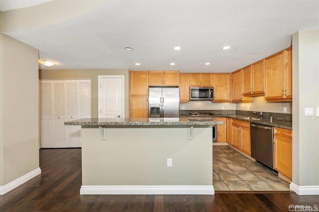 kitchen featuring dark wood-type flooring, dark stone countertops, stainless steel appliances, a kitchen breakfast bar, and a kitchen island