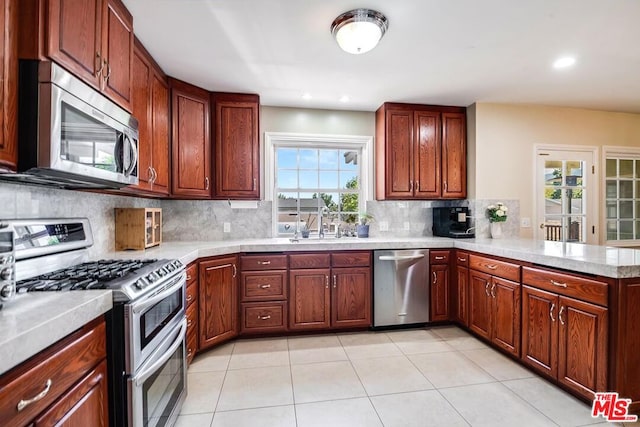 kitchen with sink, kitchen peninsula, decorative backsplash, light tile patterned flooring, and appliances with stainless steel finishes