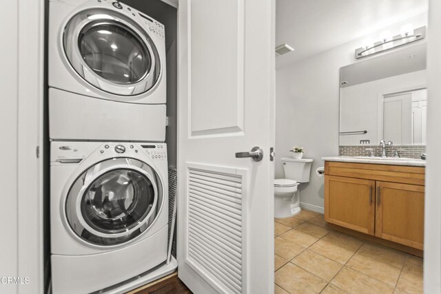 clothes washing area with light tile patterned floors, stacked washer and clothes dryer, and sink