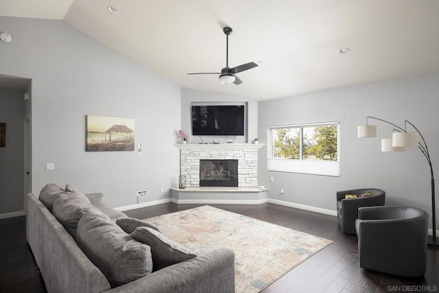 living room with ceiling fan, dark hardwood / wood-style floors, a stone fireplace, and vaulted ceiling