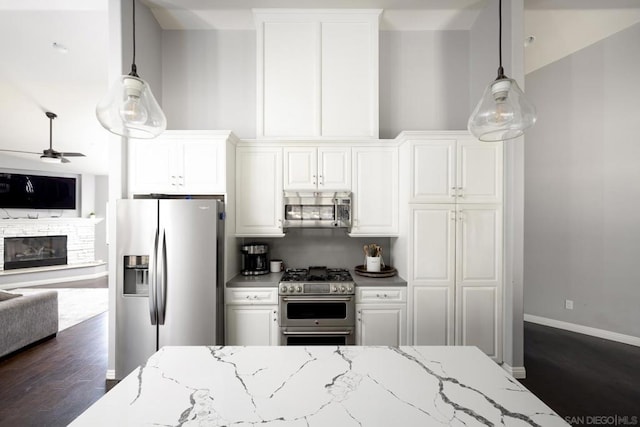 kitchen featuring white cabinetry, a stone fireplace, appliances with stainless steel finishes, hanging light fixtures, and light stone countertops