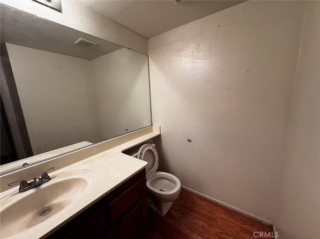 bathroom with toilet, vanity, wood-type flooring, and a textured ceiling