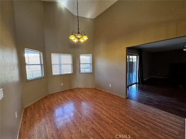 empty room with a wealth of natural light, a chandelier, hardwood / wood-style floors, and high vaulted ceiling