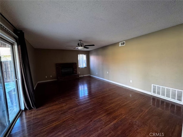 unfurnished living room featuring a textured ceiling, a brick fireplace, dark hardwood / wood-style flooring, and ceiling fan