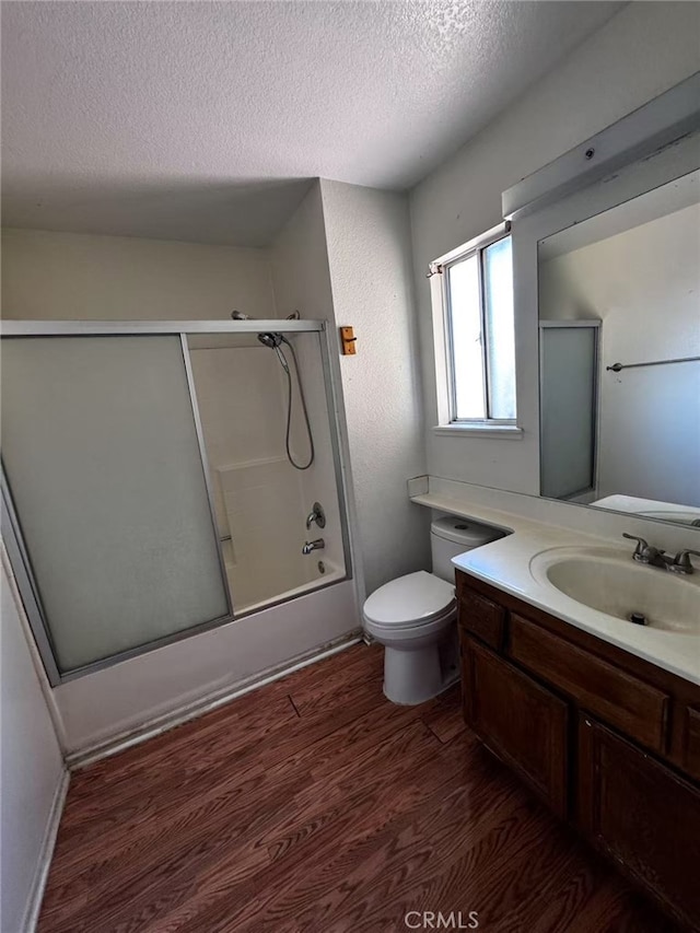 full bathroom featuring toilet, wood-type flooring, a textured ceiling, vanity, and shower / bath combination with glass door