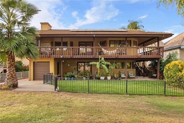 rear view of house with a garage, a wooden deck, a yard, and solar panels