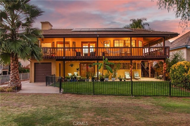 back house at dusk featuring a deck, a garage, a lawn, and solar panels