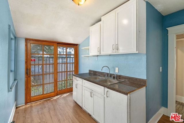 kitchen with white cabinetry, sink, light hardwood / wood-style floors, and lofted ceiling