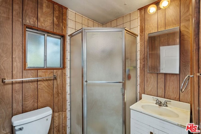 bathroom with vanity, toilet, a shower with shower door, and wood walls