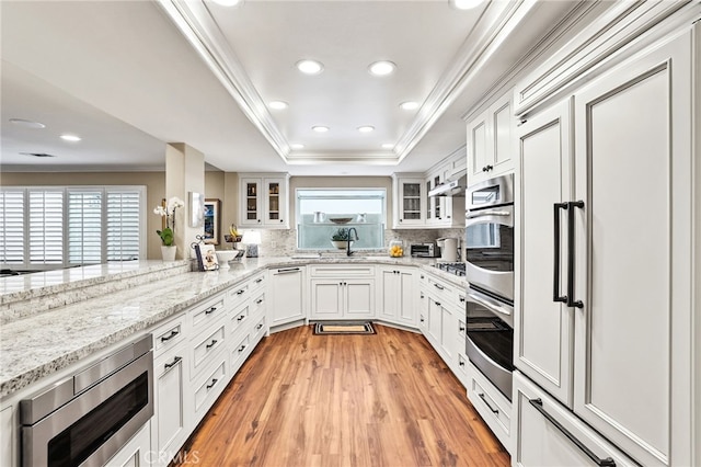 kitchen with stainless steel appliances, light stone counters, ornamental molding, white cabinets, and a raised ceiling