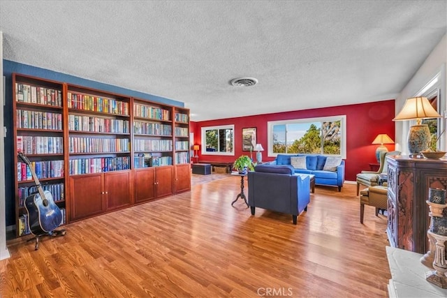 living area with visible vents, baseboards, a textured ceiling, and wood finished floors