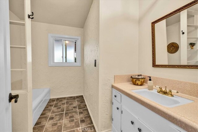 bathroom with a bath, vanity, and a textured wall