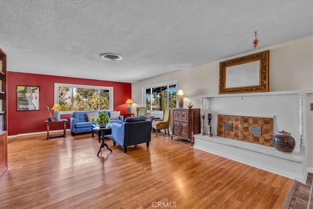 living room with wood finished floors, baseboards, visible vents, a fireplace with raised hearth, and a textured ceiling