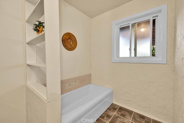 full bathroom featuring a garden tub, a textured wall, and baseboards