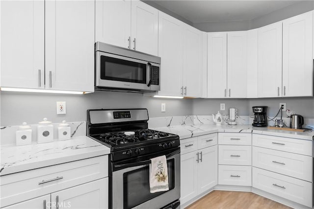 kitchen featuring stainless steel appliances, white cabinets, light hardwood / wood-style floors, and light stone counters