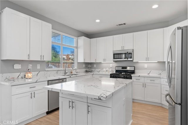 kitchen with light stone countertops, stainless steel appliances, a kitchen island, white cabinets, and sink