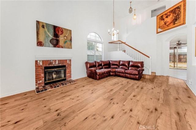 living room featuring ceiling fan with notable chandelier, hardwood / wood-style floors, a towering ceiling, and a fireplace