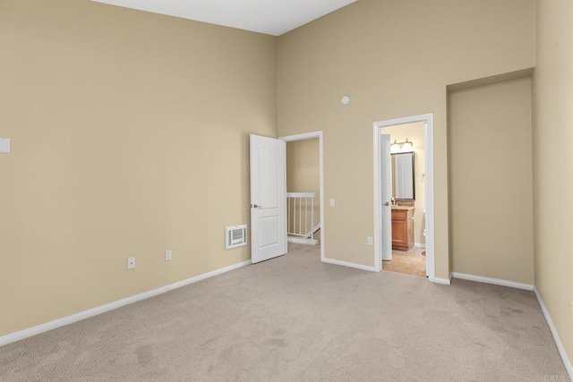 unfurnished bedroom featuring light carpet, ensuite bathroom, and a high ceiling